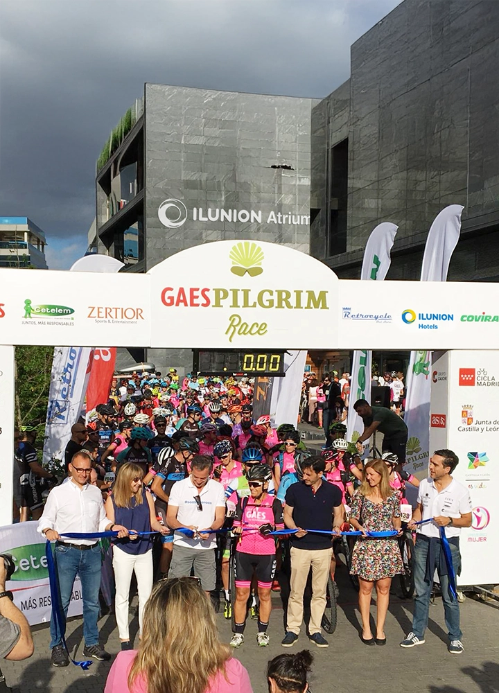 Grupo de ciclistas y autoridades en la línea de salida de la GAES Pilgrim Race frente al edificio ILUNION Atrium.