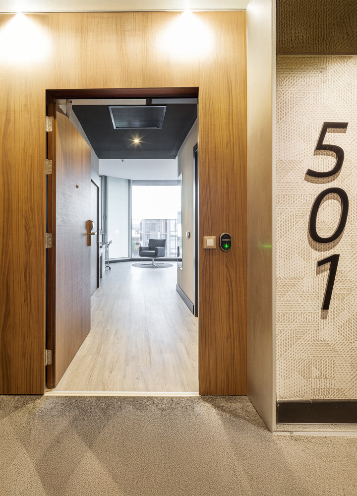 Open door of room 501 with light wooden floor, large window, and modern furniture inside.