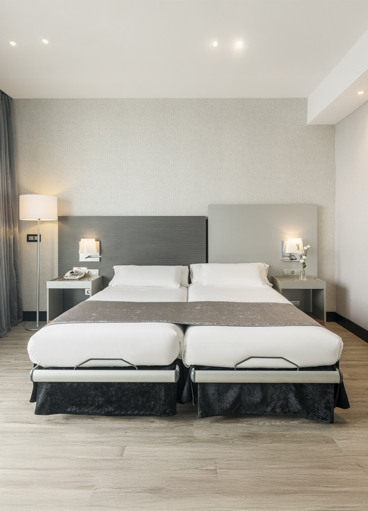 Modern hotel room with two twin beds pushed together, minimalist decor, wooden floor, and bedside lamps.