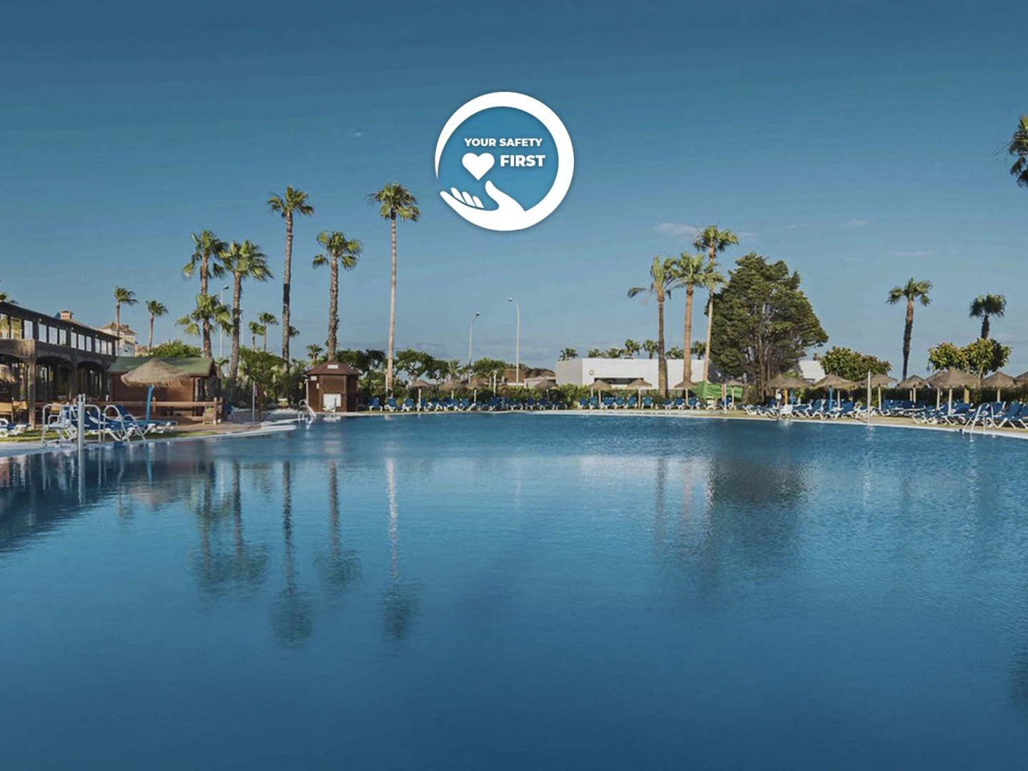 Hotel con piscina al aire libre con agua clara. Con un logo de una mano en el centro que tiene el texto "YOUR SAFETY FIRST"