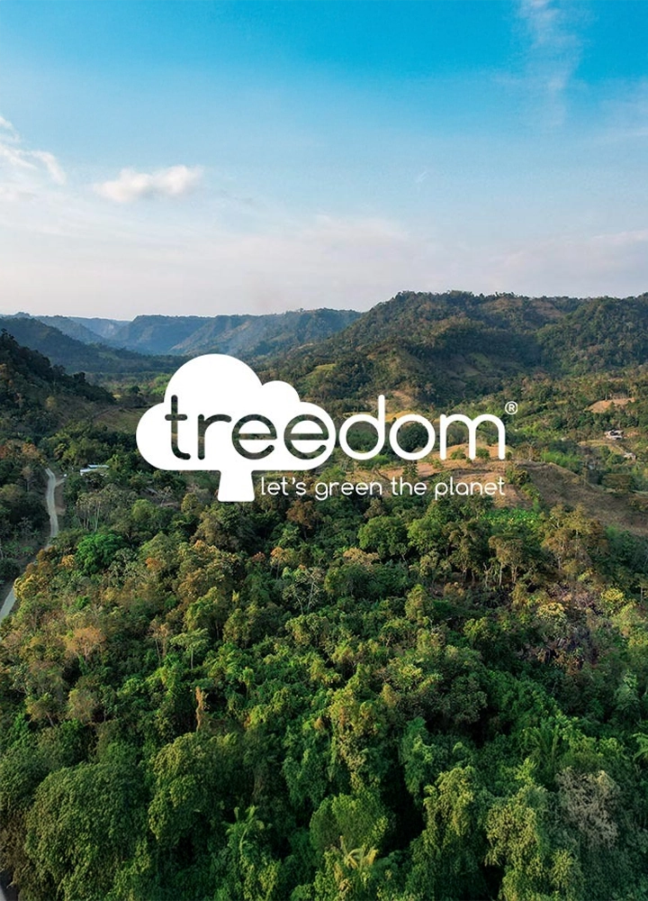 Paisaje verde con colinas y muchos árboles bajo cielo claro. Un logo en forma de árbol dice “treedom” y el lema “let’s green the planet”.