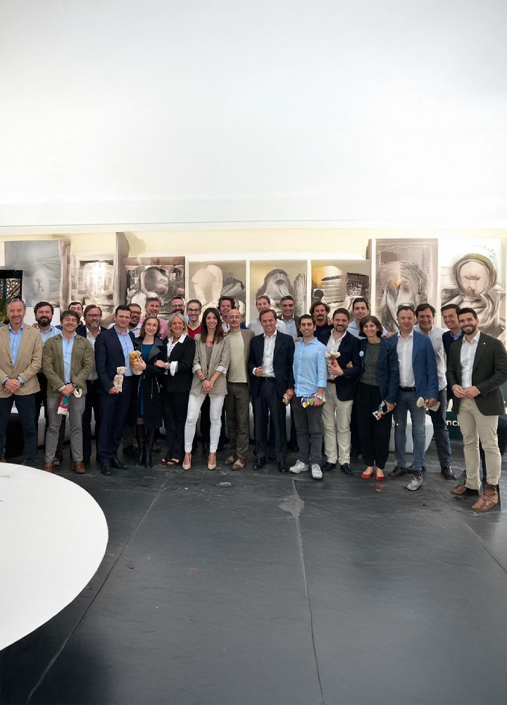 Grupo de personas con ropa formal, posan sonrientes en un espacio interior artístico.