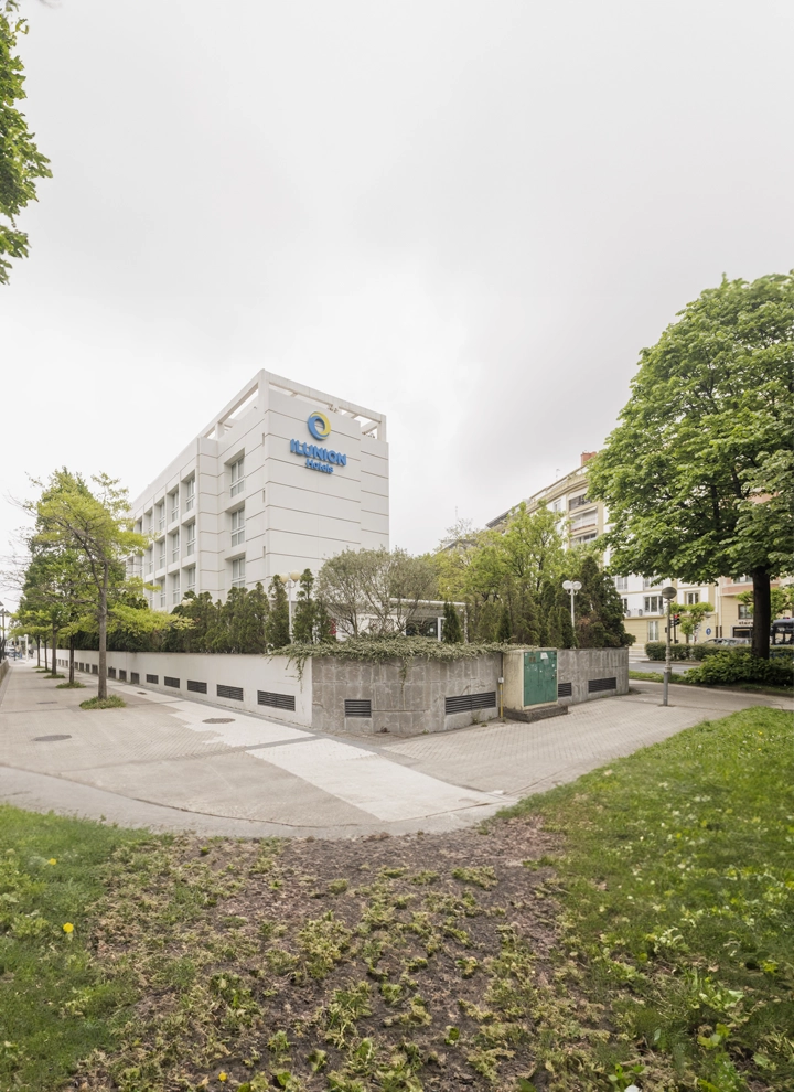 En la imagen se puede ver la fachada blanca del hotel ILUNION San Sebastián rodeado de árboles de hoja verde.