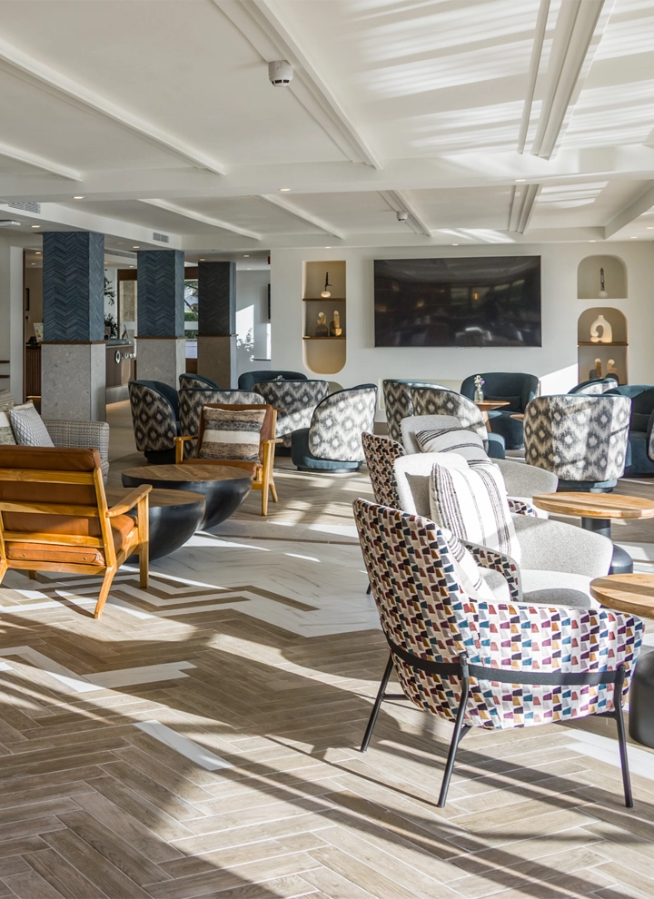 La imagen muestra una sala de estar moderna, espaciosa y elegante con una variedad de opciones de asientos. La habitación presenta una combinación de elementos de diseño contemporáneo y moderno de mediados de siglo, caracterizada por líneas limpias, patrones geométricos y una mezcla de texturas.