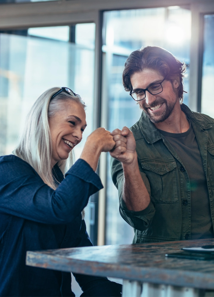 Dos personas chocando sus puños con complicidad. El entorno parece ser interior, posiblemente una oficina.