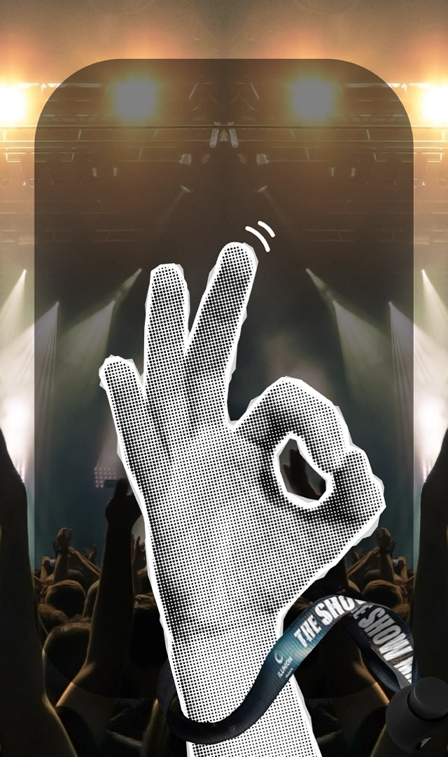 Imagen de una mano con una pulsera, haciendo el gesto de "ok" en primer plano, sobre un fondo borroso de un escenario.