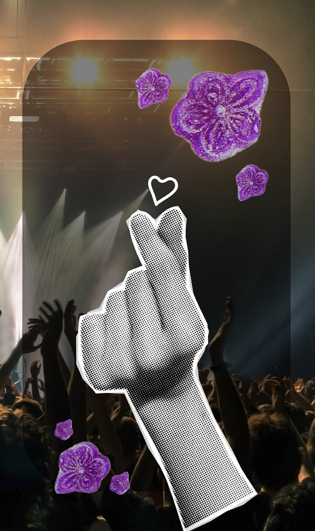 Mano haciendo un gesto de corazón con los dedos, rodeada de flores moradas y sobre un fondo borroso de un concierto.