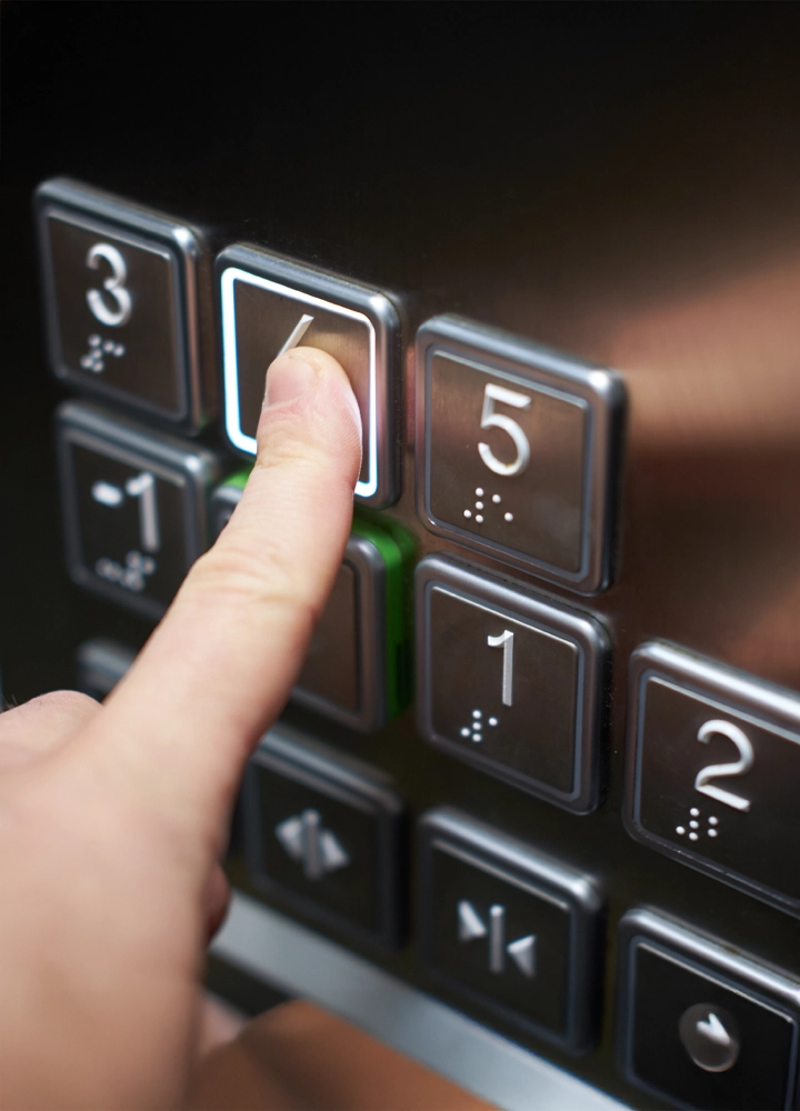 Primer plano de una mano presionando el botón número cinco en un panel de control de un elevador.