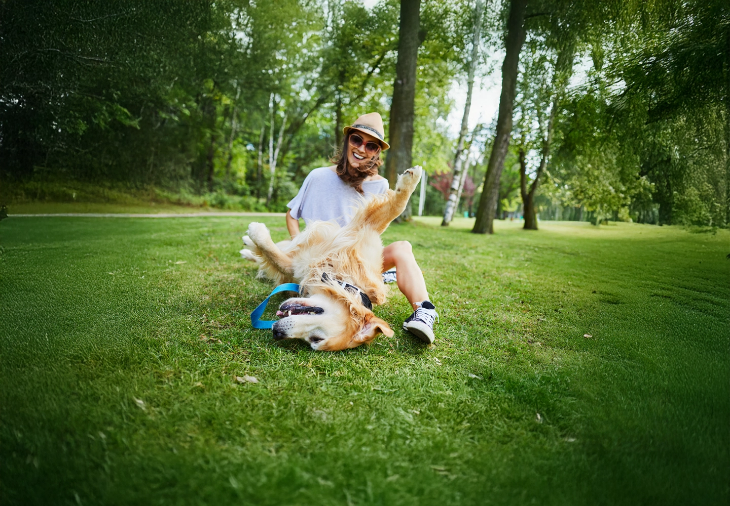 Mujer jugando en un parque, con su mascota, en un día soleado.
