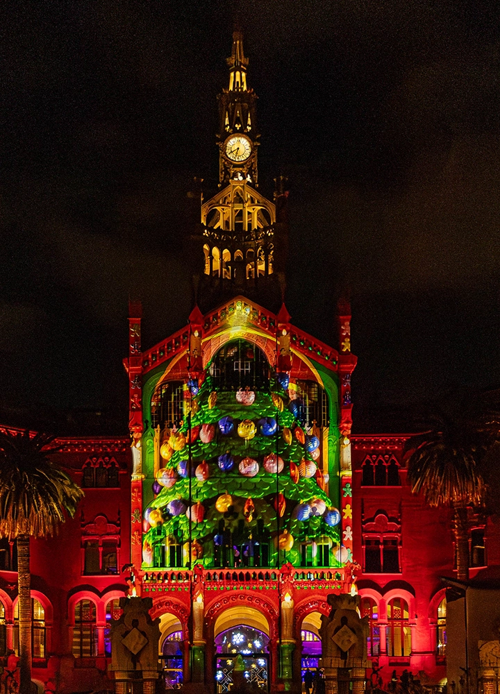 Monumental edificio de Barcelona iluminado con distintos tonos: rojos, azules... que anuncian la llegada de las fiestas de Navidad.