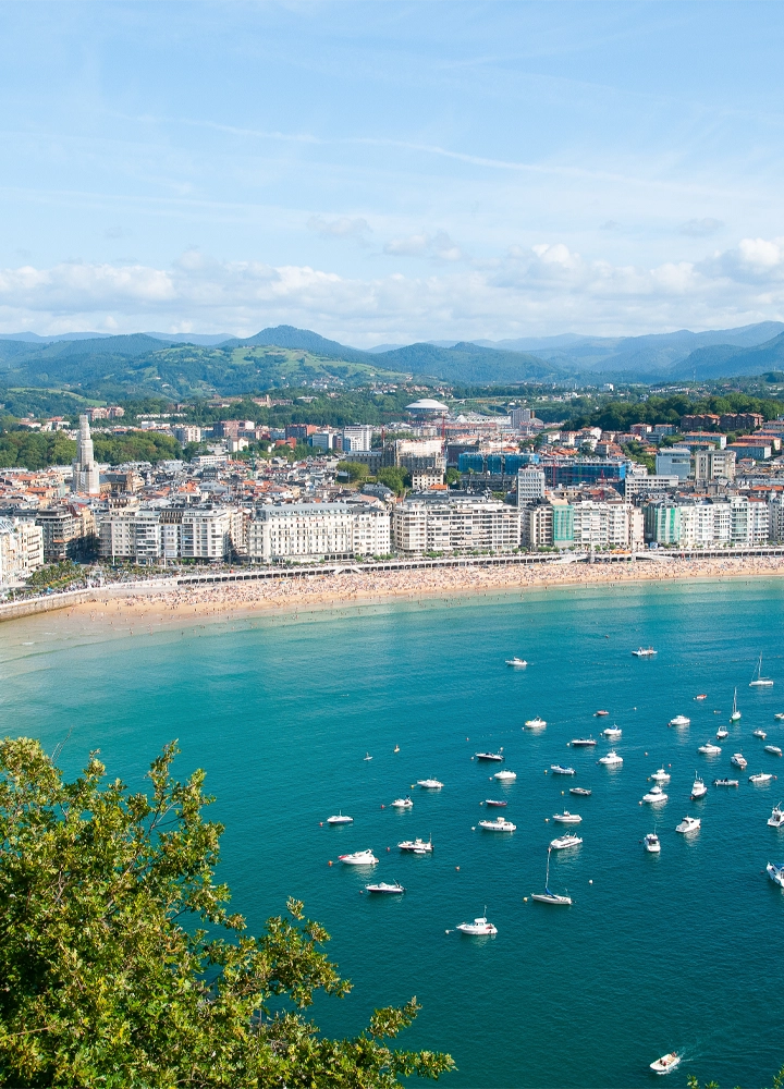 Fotografía panorámica de una ciudad costera, mostrando una playa de arena blanca, un puerto lleno de barcos y edificios a lo largo de la costa.