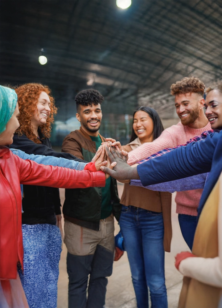 Un grupo diverso de personas de distintos géneros y etnias se reúne en una oficina sonriendo. Transmite unión y un fuerte sentido de comunidad en un entorno laboral.