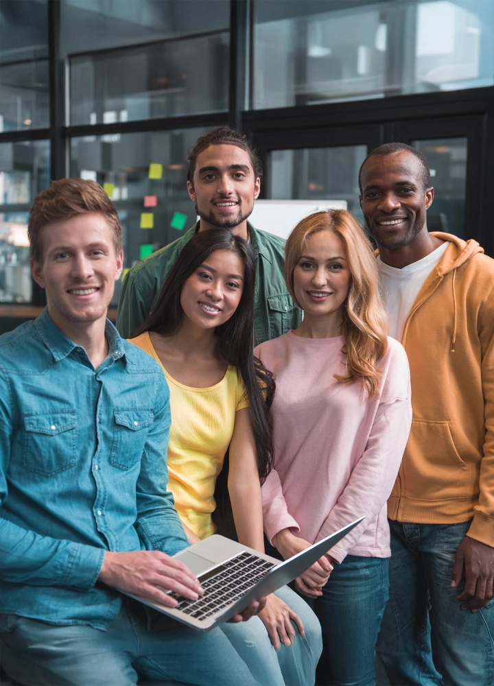 Un grupo diverso de personas de distintos géneros y etnias se reúne en una oficina sonriendo. Transmite unión y un fuerte sentido de comunidad en un entorno laboral.