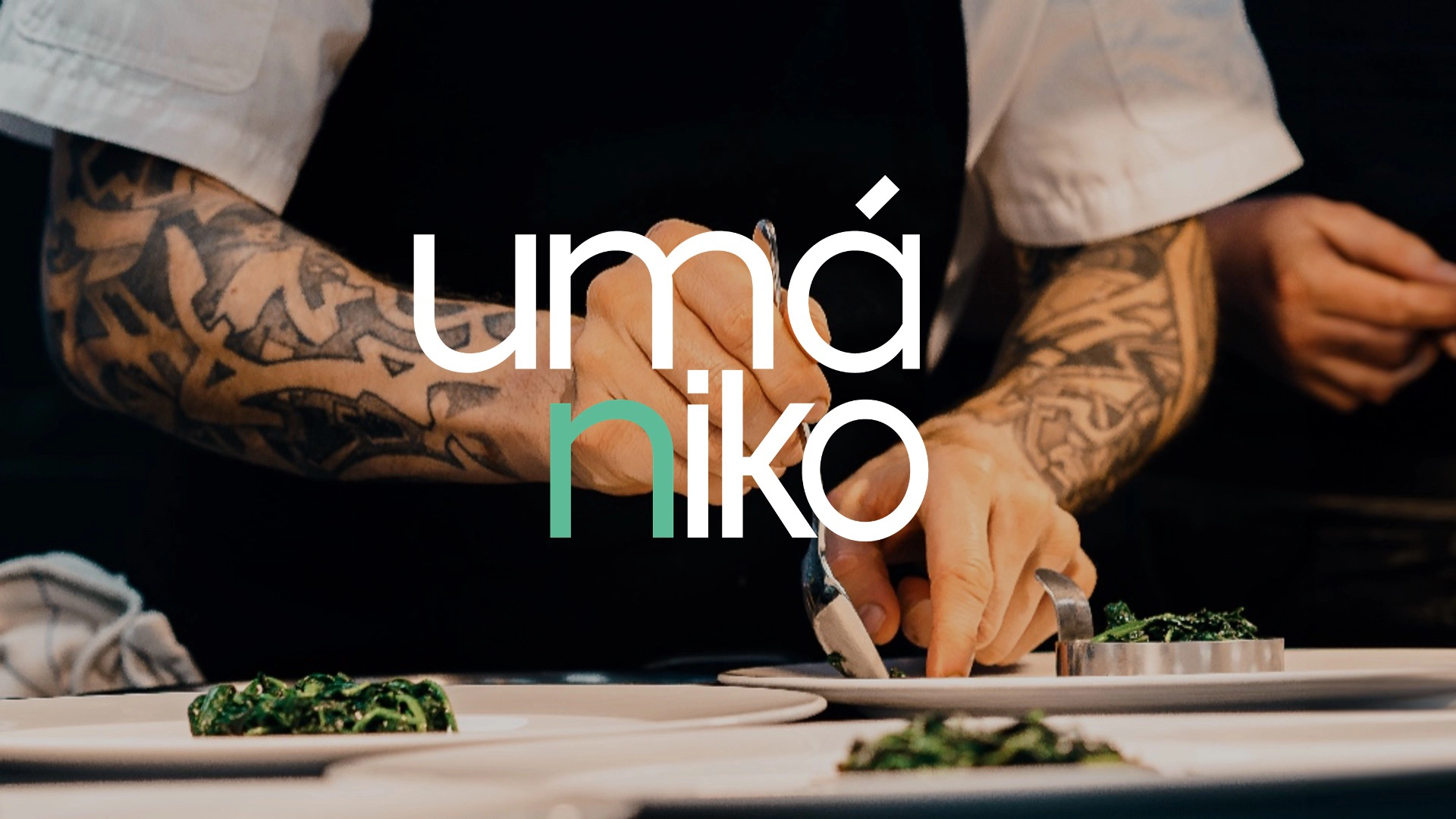 Primer plano de manos tatuadas de un chef emplatando comida con precisión. El texto 'umániko' aparece en tipografía moderna, con las letras 'nik' en color verde, destacando el nombre del restaurante o marca.