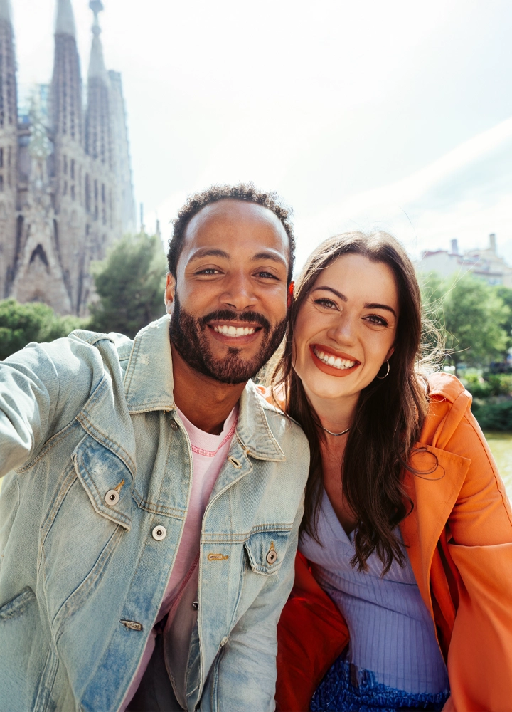 Pareja joven tomándose una selfie frente a la Sagrada Familia, disfrutando de un día soleado.