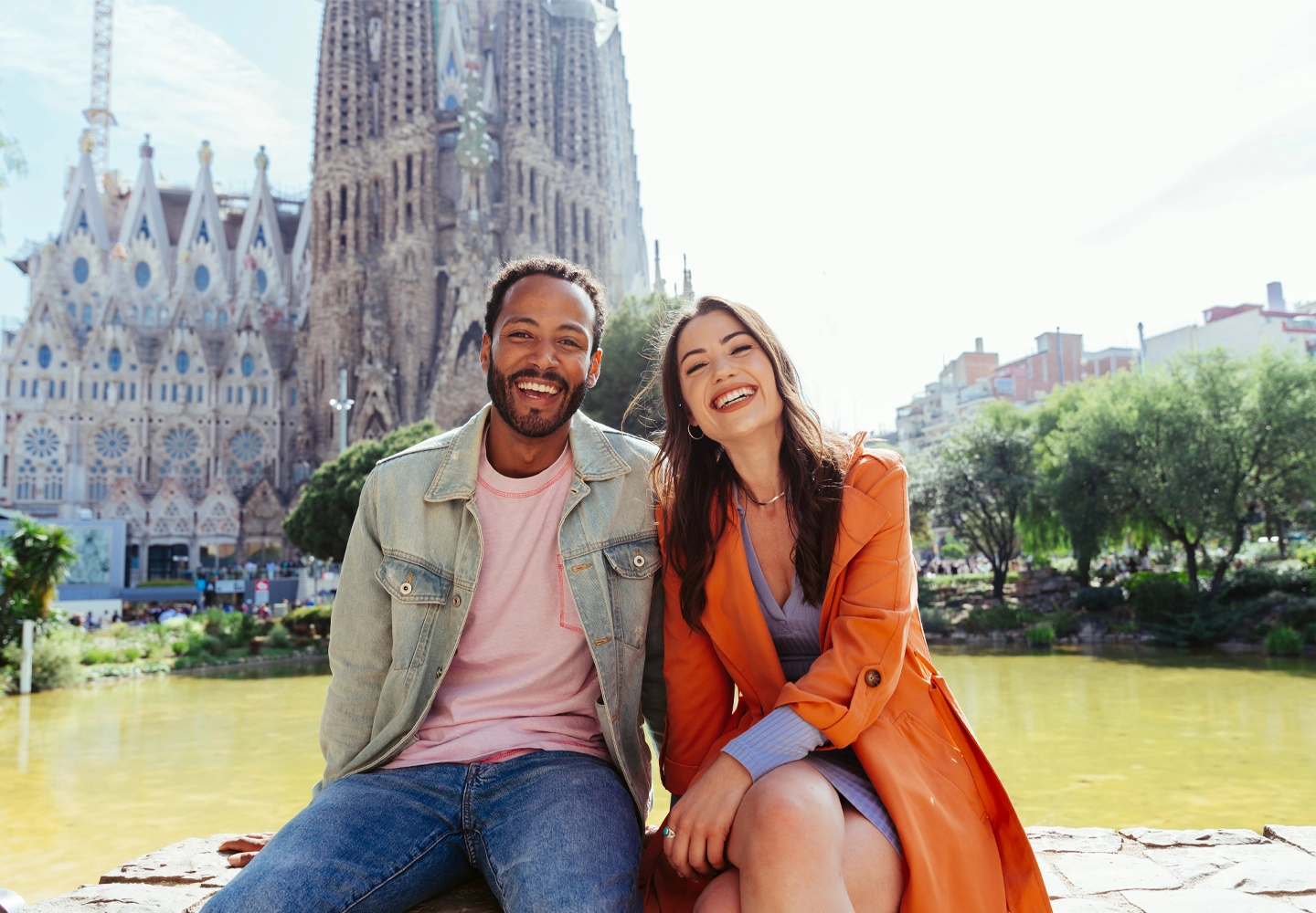Pareja sentada frente a la Sagrada Familia, sonriendo y disfrutando de un momento juntos.