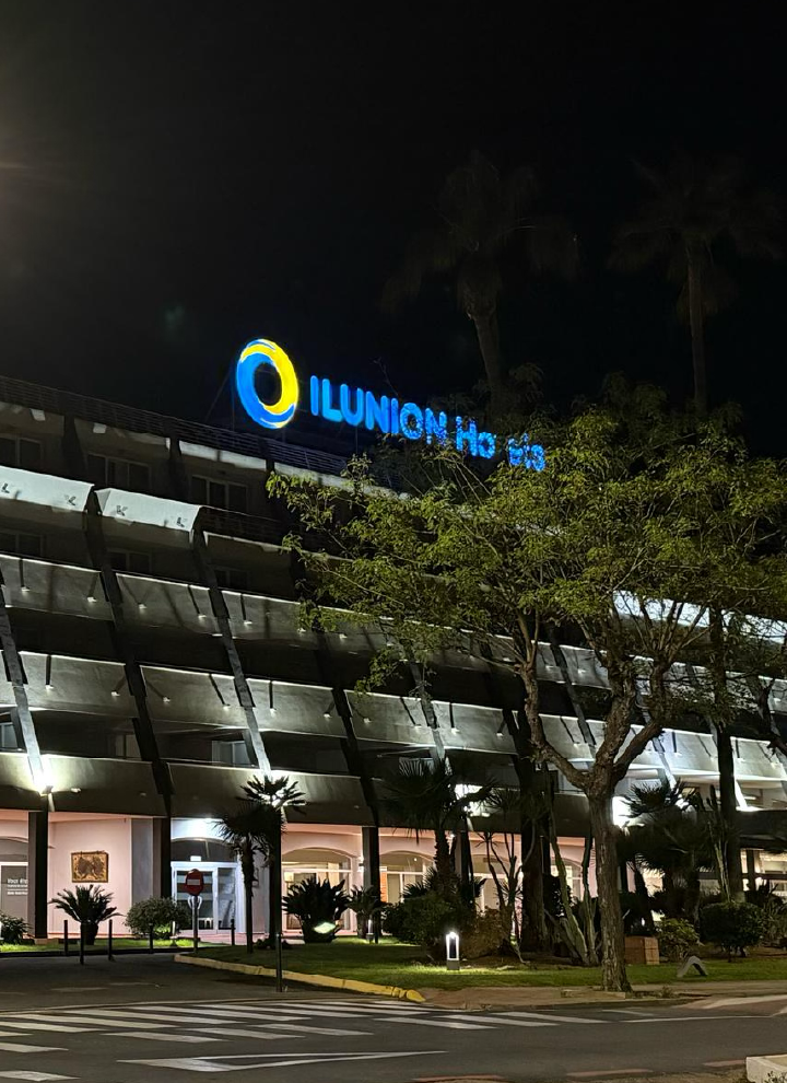 edificio moderno de varias plantas iluminado durante la noche. En la parte superior del edificio se puede ver el letrero iluminado con el texto 