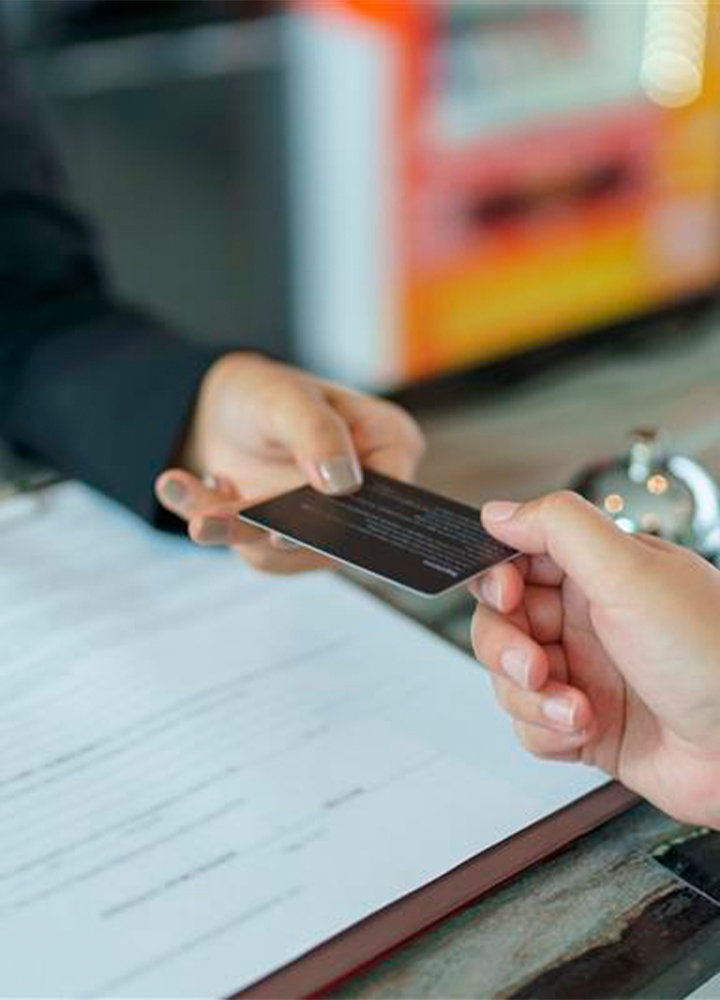 Una mano extiende una tarjeta a otra persona sobre una mesa con papeles.
