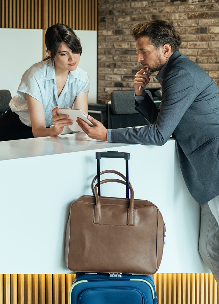 Hombre hablando con una recepcionista, y dos maletas apoyadas en el mostrador.