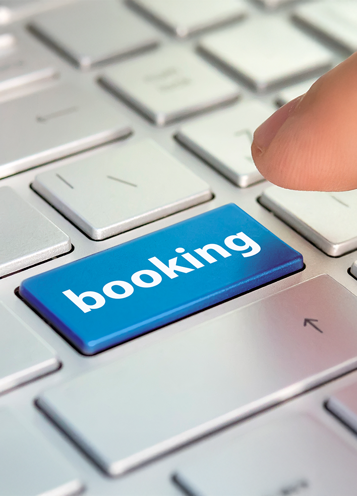 Un dedo está a punto de presionar una tecla azul de ordenador que dice “booking”.