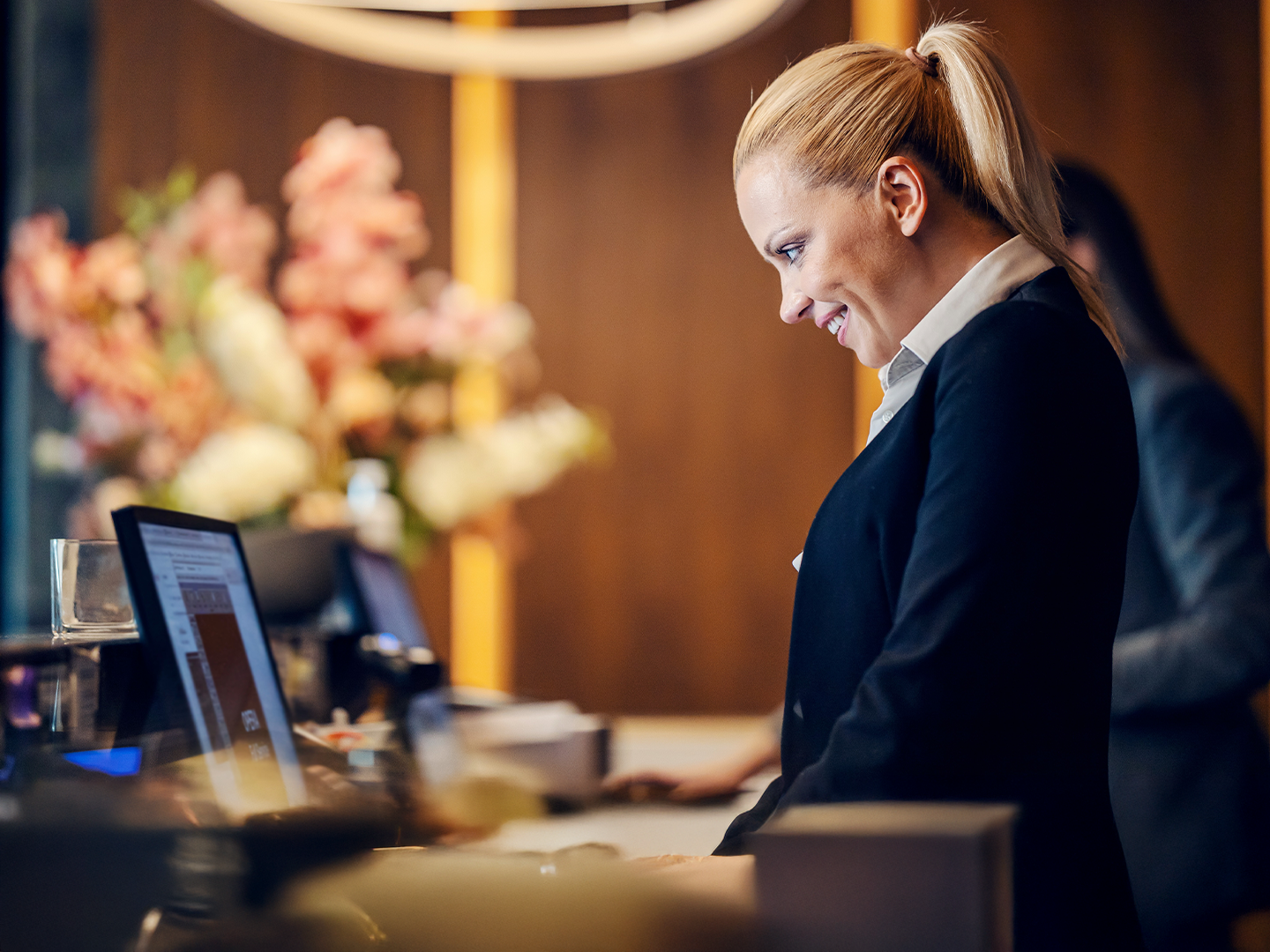 Mujer con cabello rubio de pie en un mostrador trabajando en un portátil.