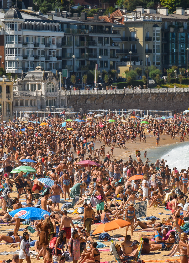 Playa abarrotada de personas pegadas junto a sombrillas de colores.
