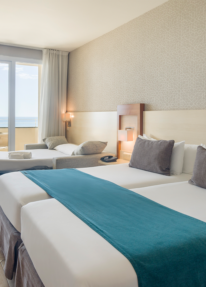 Habitación de hotel con dos camas individuales y una cama auxiliar en el sofá.