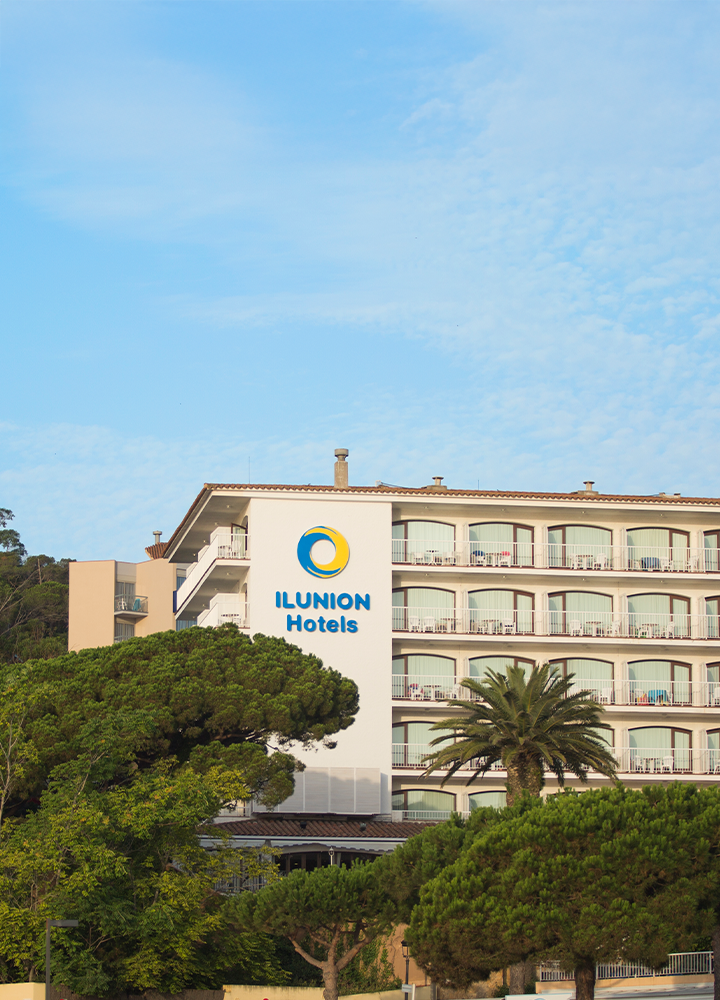 Hotel ILUNION Caleta Park con balcones en varias plantas, rodeado de árboles verdes.