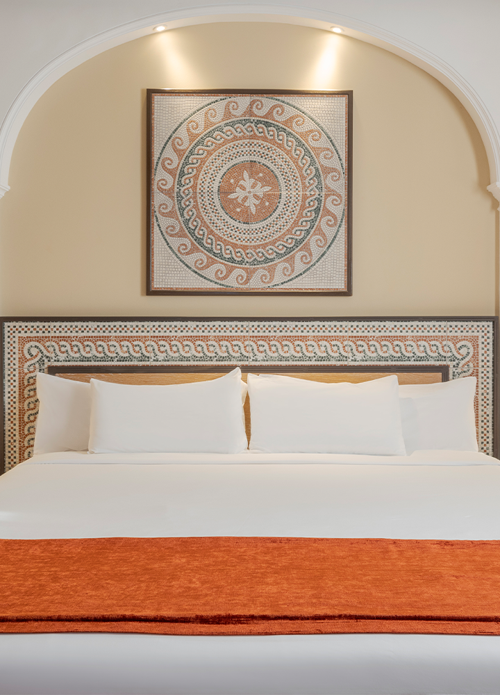 Cama grande y espaciosa con una manta de tono naranja extendida sobre la cama y un cabecero con formas geométricas.