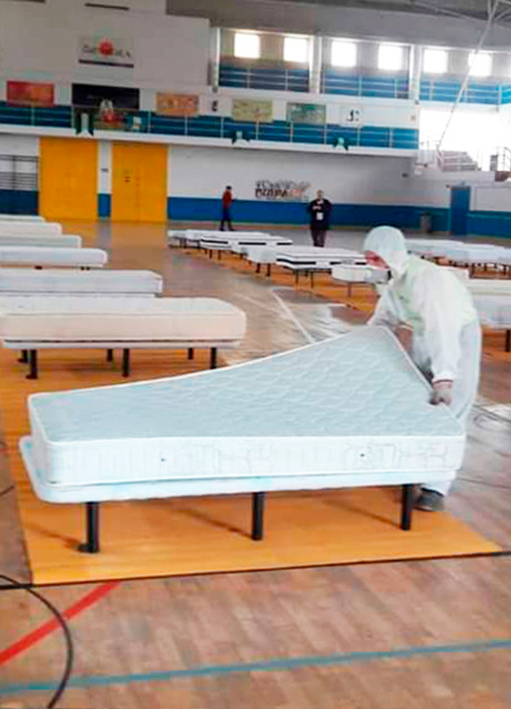 Gimnasio grande convertido en un espacio de emergencia con varias camas individuales alineadas en filas.