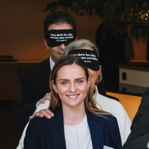 Several people are taking part in an activity, some wearing blindfolds that read “To open your eyes, you just have to close them.” A woman at the front is smiling.