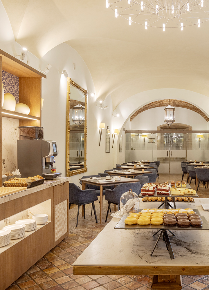 Comedor elegante con un ambiente acogedor. Hay una estación de servicio con una máquina de café y varios platos y tazas. En el centro, hay una mesa grande con una variedad de dulces.
