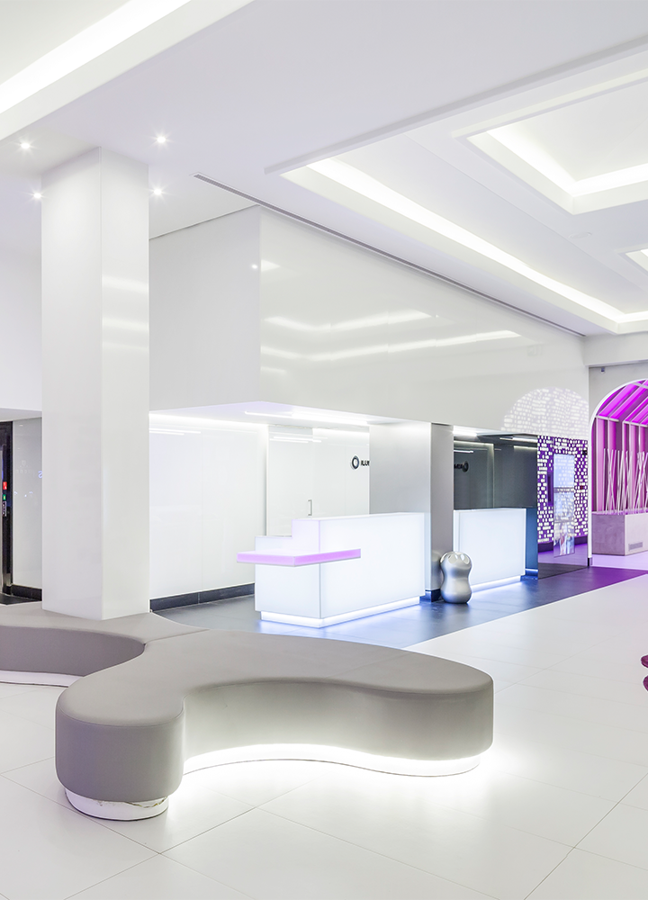 Recepción moderna y amplia, con luces moradas, un sofá curvo y formas arquitectónicas