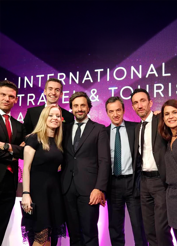 Grupo de personas vestidas de manera elegante, posando juntas en un evento. En el fondo, se lee el texto 