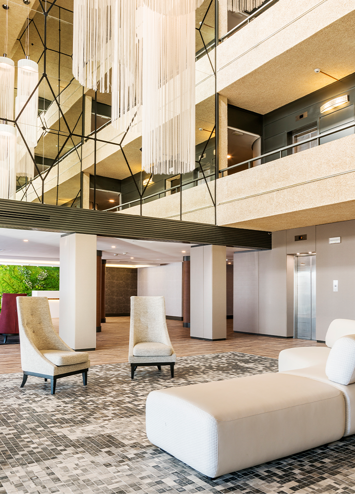 Recepción con sofás blancos, alfombra decorativa, columnas y lámparas colgantes del techo.