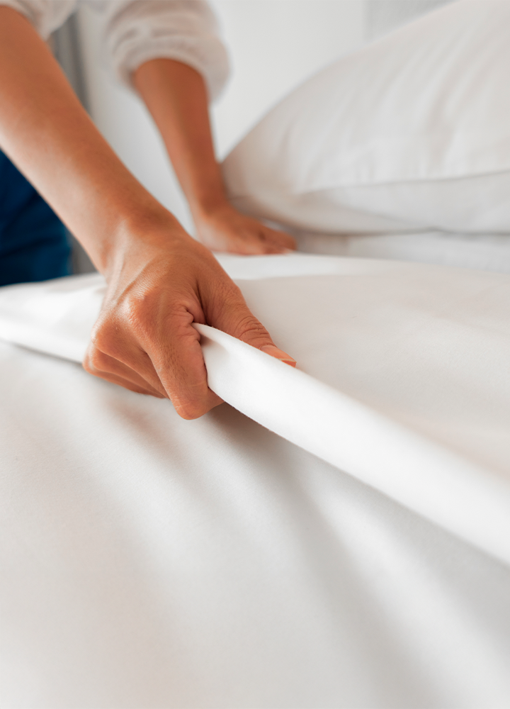 Una mano estira una sábana blanca sobre una cama.