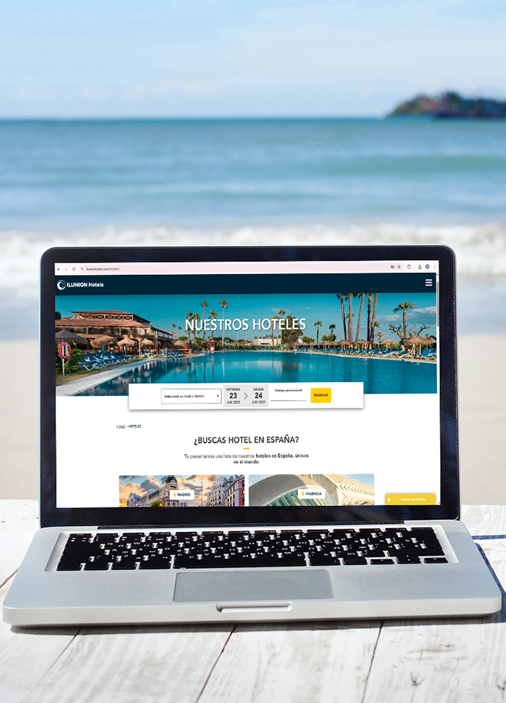 Un portátil abierto sobre una mesa frente al mar muestra la página web de ILUNION Hotels con un buscador de fechas.