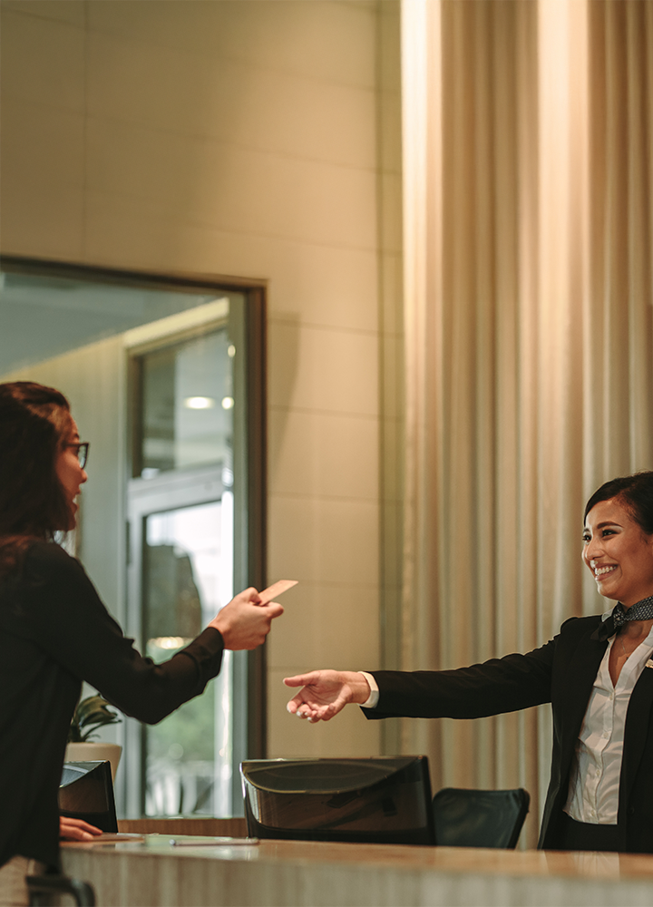 Persona entregando una tarjeta a una recepcionista en un hotel.