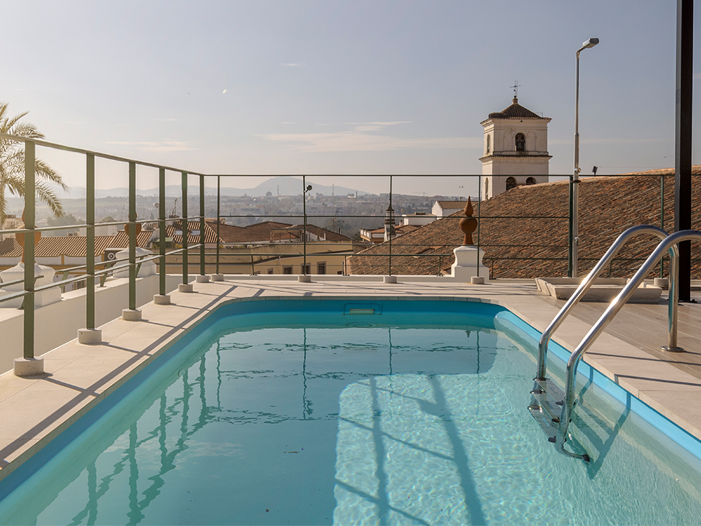Piscina en la azotea del hotel. Es una piscina rectangular con agua azul clara. Hay una escalera de metal que permite entrar y salir del agua.