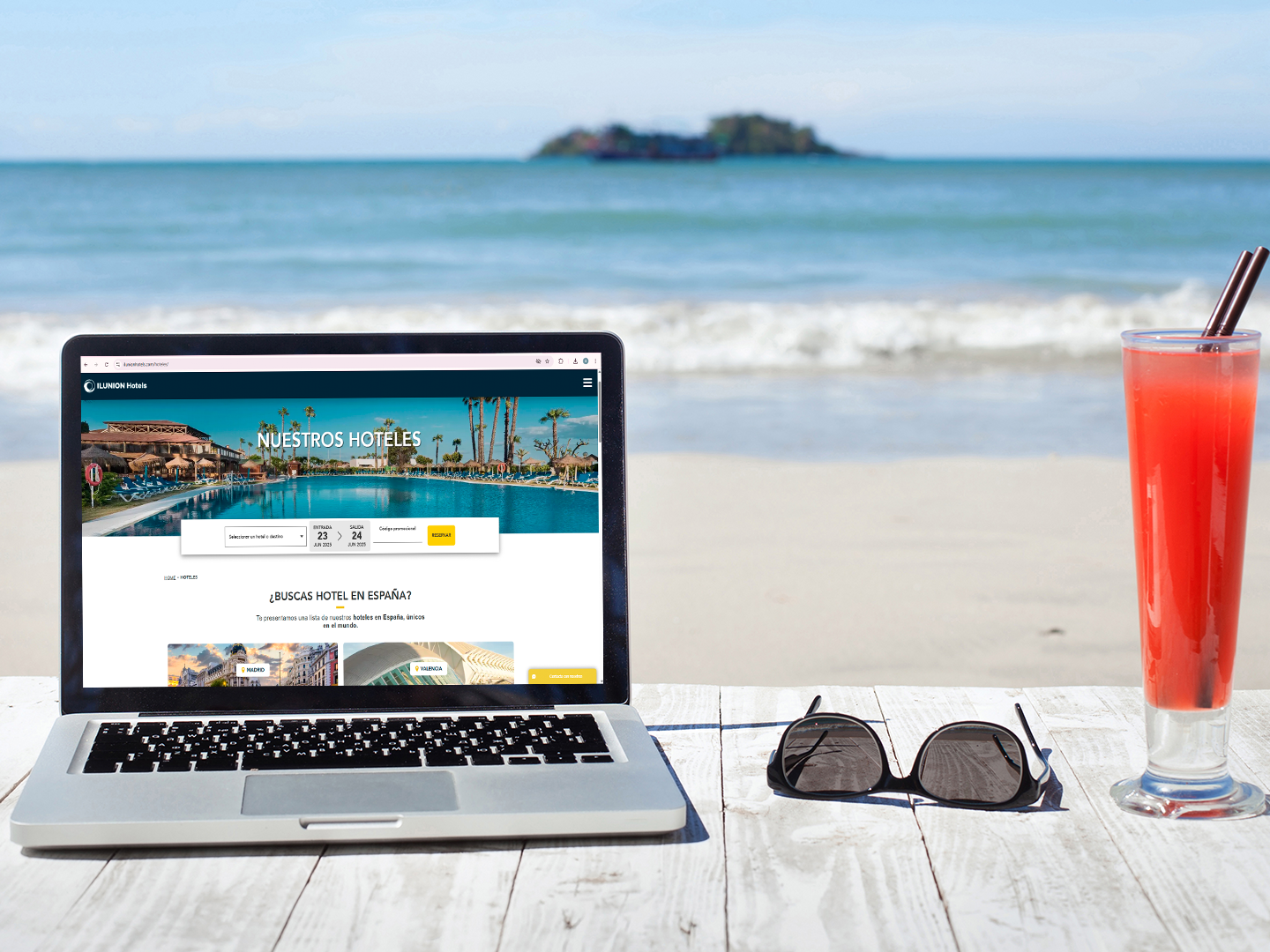 Un portátil abierto sobre una mesa frente al mar muestra la página web de ILUNION Hotels con un buscador de fechas.
