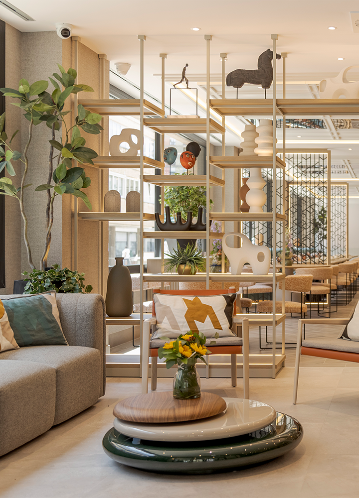 Interior de un hotel con estanterías, plantas, sillones y una mesa con flores
