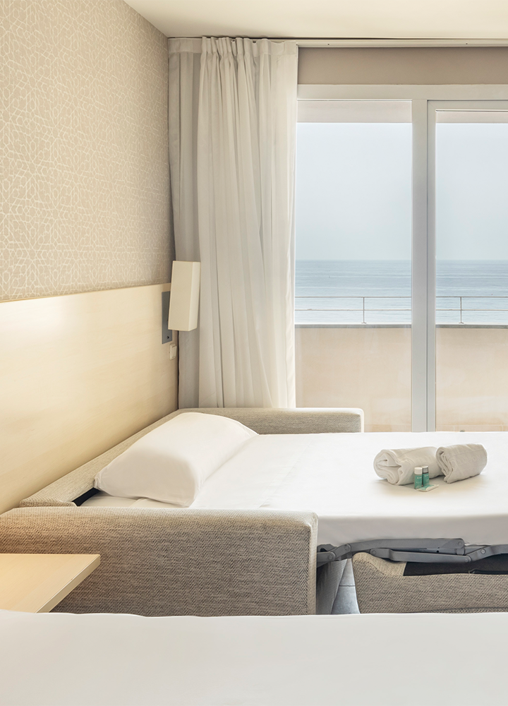 Habitación de hotel con una cama individual auxiliar. La cama está hecha con sábanas blancas y tiene una almohada blanca.