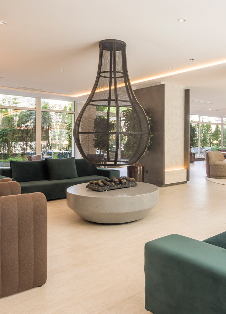 Espacio interior de hotel con sofás verdes y marrones y una gran chimenea abstracta en medio.
