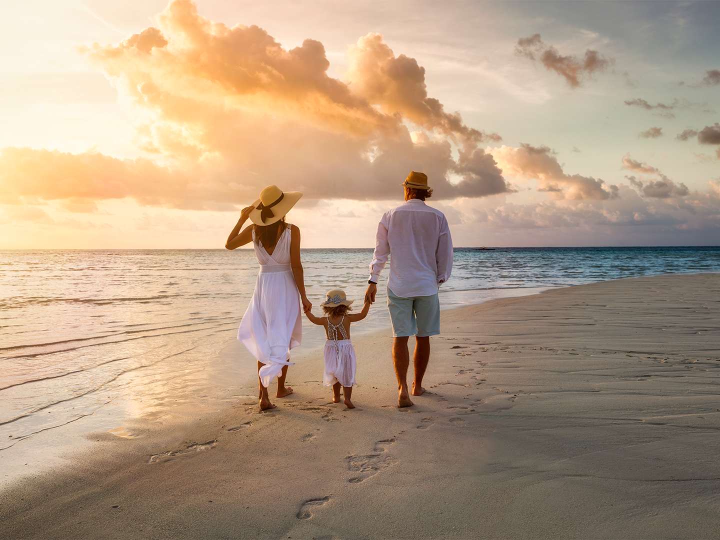 Familia caminando por la playa al atardecer, con el mar y el cielo nublado de fondo.
