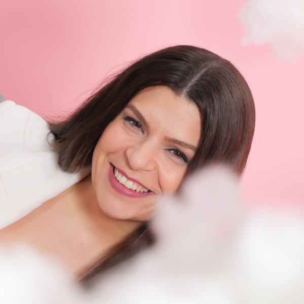 ChatGPT Plus The image features a woman with long, dark hair, smiling brightly. She is wearing a white blazer over a red top. The background is a soft pink tone that conveys warmth.