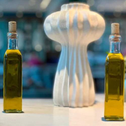 Transparent glass bottle filled with golden olive oil, with a cork stopper, on a well-lit countertop.