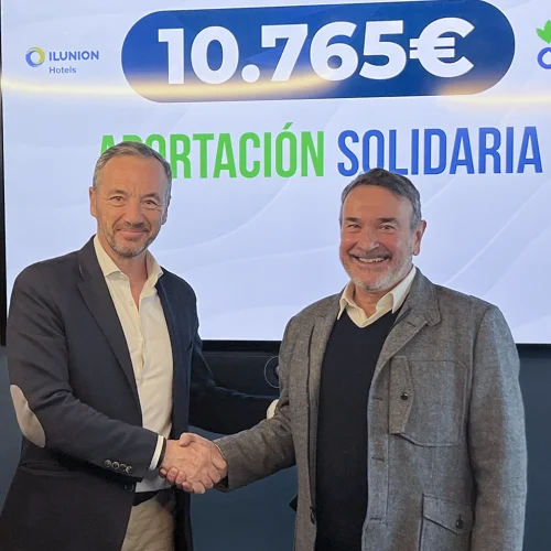 Two people shake hands in front of a screen displaying the text “ILUNION Hotels”, “€10,765” as a charitable contribution, and “ACTION AGAINST HUNGER”.