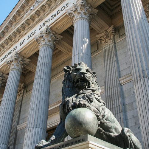 Main façade of the Congress of Deputies in Madrid, featuring its iconic Corinthian columns and the bronze lions guarding the entrance—symbols of popular sovereignty in Spain.