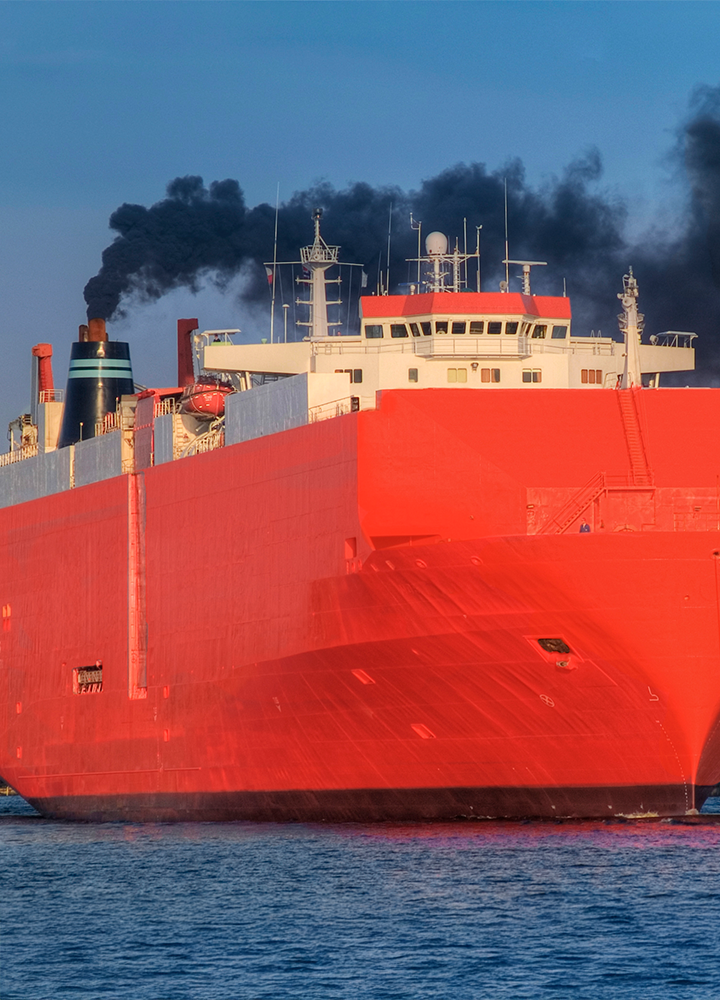 Gran barco rojo navega por el agua mientras sale humo negro de su chimenea.