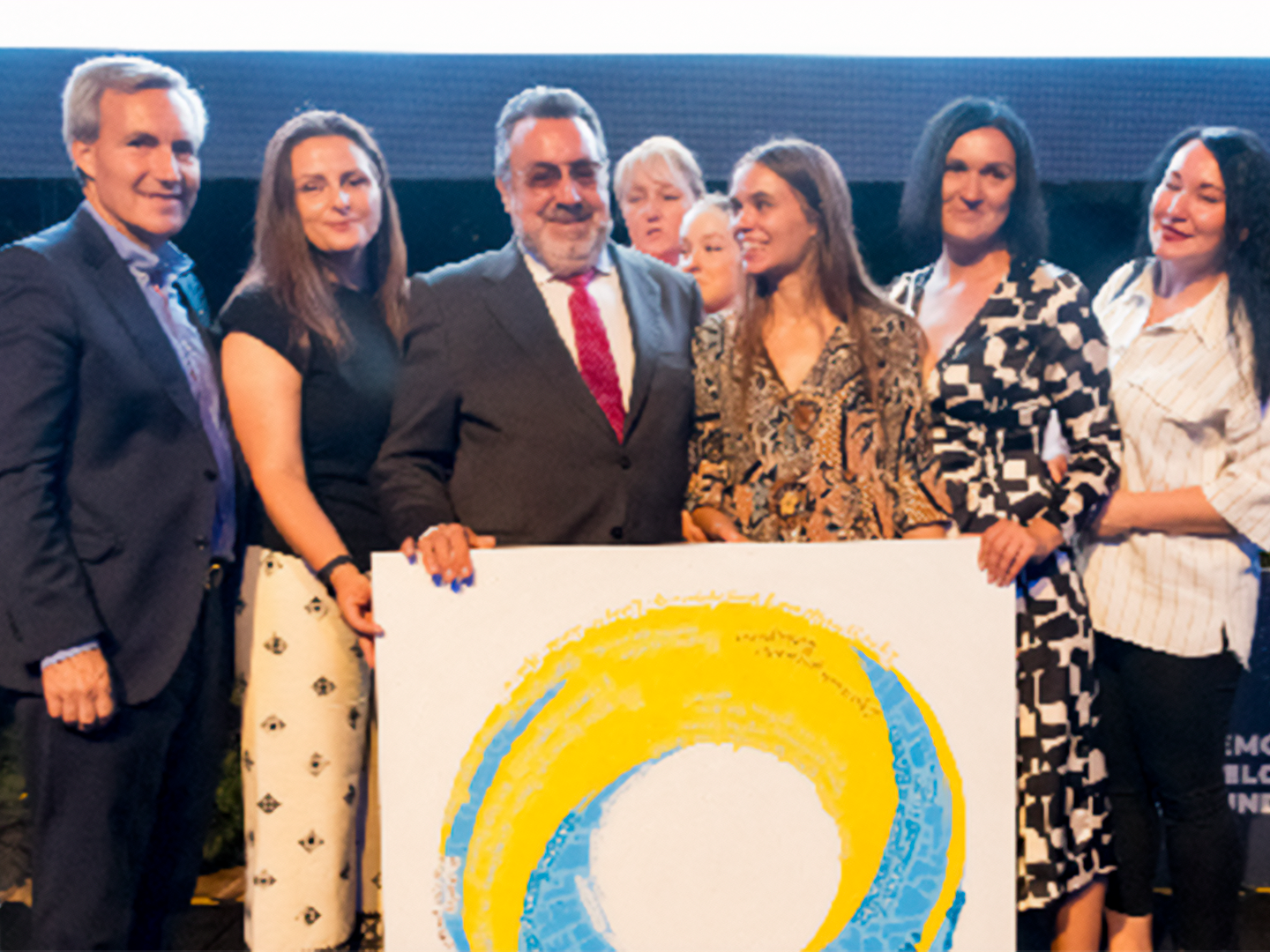 Seis personas, vestidas elegantemente, posan juntas sosteniendo un gran cuadro circular de colores azul y amarillo que representa el logo de ILUNION Hotels.